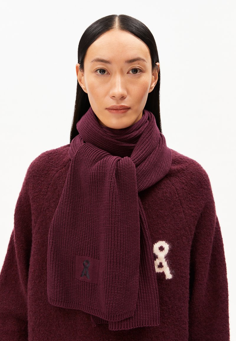 Bordeaux gebreide sjaal met een textuur ribbelpatroon, voorzien van een klein logo patch. Complementair aan een zachte, bordeaux trui.