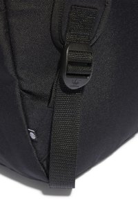 Black fabric bag featuring a textured surface, adjustable strap with a plastic buckle, and a small logo tag. Compact design with a side pocket.