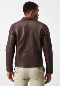 Brun läderjacka med en skräddarsydd design, dekorativ sömnad och dragkedjestängda ärmar, visad bakifrån mot en enkel bakgrund.
