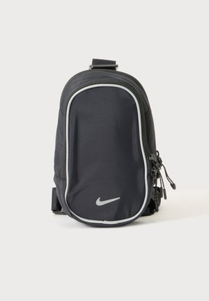 Sac banane Nike noir compact avec plusieurs compartiments zippés et une poche avant bordée de blanc, présenté sur un fond clair uni.
