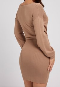 Robe en maille côtelée beige douce, avec manches longues et silhouette ajustée, mettant en valeur la texture et la forme avec un ourlet légèrement incurvé.