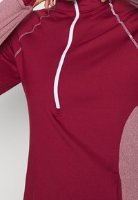 Maroon pitkähihaine paita, jossa on puolivetoketjumuotoilu, kontrastiväriset vaaleanpunaiset hihat, litteät saumat ja sileä pinta.