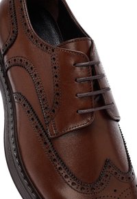Brązowe skórzane buty wizytowe z detalami brogue, okrągłym noskiem i ciemnobrązowymi sznurowadłami na czarnej podeszwie.
