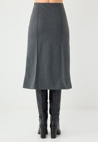 Grauer Woll-Midi-Rock mit ausgestellter Form, der über schwarzen kniehohen Stiefeln getragen wird. Glatte Textur, minimalistisches Design.