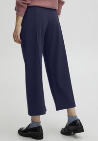 Navy wijde broek gemaakt van een zachte stof, met een eenvoudig ontwerp en een relaxte pasvorm, gecombineerd met zwarte schoenen en blauwe sokken.