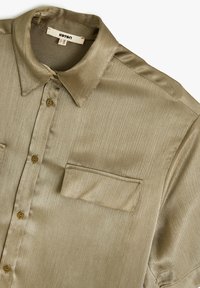 Beige shirt met korte mouwen, gemaakt van een gladde stof. Heeft een knoopsluiting aan de voorkant, een puntkraag en een borstzak met een gestructureerde afwerking.