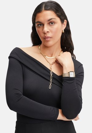 Top noir à manches longues avec un design décolleté, en tissu superposé, associé à un collier en chaîne dorée et une montre en argent avec un bracelet en maille.