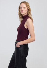 Bordeaux mouwloos top met hoge hals, gemaakt van rekbare stof, gecombineerd met zwarte leren broek met zijzakken en een aansluitend ontwerp.