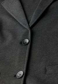 Blazer gris en tissu texturé. Doté de revers crantés, de deux boutons noirs portant l'étiquette "CECIL" et d'une poche poitrine unique.