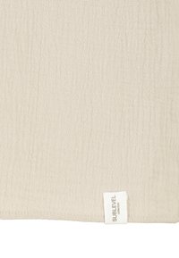 Beige-texturiertes Gewebe mit einem dezenten Kräuselungsmuster, versehen mit einem kleinen weißen Etikett mit der Aufschrift "SUBLEVEL" am unteren Rand.