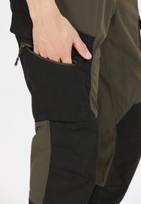 Cargo broek met een combinatie van donkergroen en zwart materiaal, met zichtbare ritszak en versterkte stiksels.