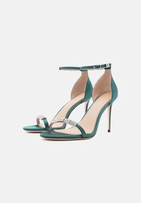 Tyrkysové saténové sandály na vysokém podpatku s náramkem kolem kotníku, vyznačující se archovou páskou s akcenty z rhinestones a špičatou špičkou.