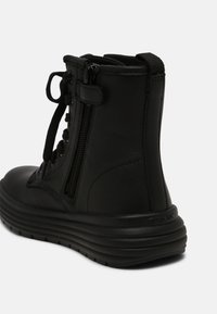 Bottine noire en cuir avec fermeture éclair latérale, lacets à l'avant, languette à l'arrière et semelle épaisse rainurée.