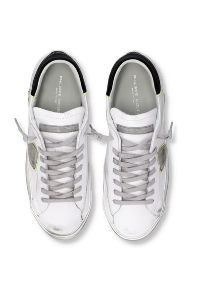 Zapatillas de cuero blancas con cordones grises, acentos en negro y amarillo neón. Presentan un diseño lateral texturizado y un collar acolchado.