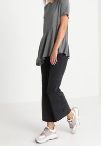 Šedý krátký rukáv peplum top, kombinovaný s černými rozšířenými džíny a bílými teniskami s šedými a oranžovými akcenty. Hladká textura po celém oblečení.
