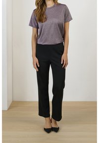 Svarta skräddarsydda byxor i kombination med en glittrande lila kortärmad topp. Toppen har en rund halsringning och en slät, texturerad yta.