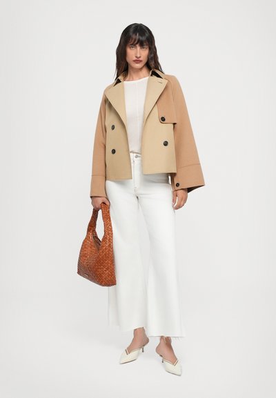 Beige cropped double-breasted coat, black buttons, paired with white wide-leg jeans, cream top, and woven brown handbag. Pointed white pumps.