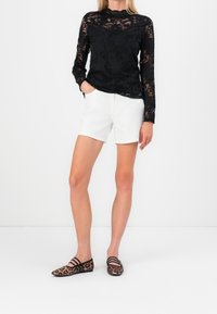 Top lungo a maniche nere in pizzo con motivo floreale, abbinato a pantaloni corti bianchi, valorizzato da ballerine con stampa leopardata e fasce nere.