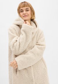 Beige teddyjas met capuchon, van textuur fleece materiaal, oversized pasvorm en brede mouwen, met een eenvoudig ontwerp zonder sluitingen.