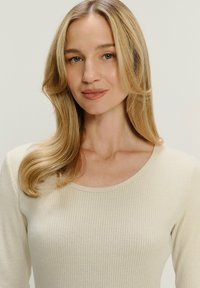 Top ribbed beige chiaro con scollatura rotonda e maniche lunghe, caratterizzato da una texture morbida e una leggera lucentezza.
