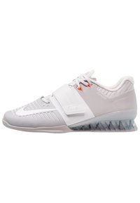 Grå træningssko med en mesh-overdel, en segmenteret gennemsigtig sål og en rem over midtfoden. Har orange detaljer og teksturerede sektioner.