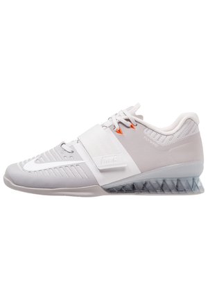 Grijze trainingsschoenen met een bovenwerk van mesh, een gesegmenteerde doorzichtige zool en een band over de middenvoet. Gekenmerkt door oranje accenten en textuurelementen.