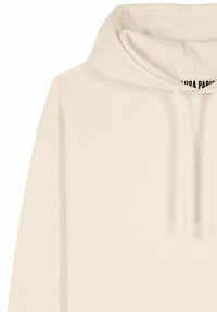 Bež pulover s kapuco z vrvicami in vidno delno etiketo znotraj ovratnika, izdelan iz mehkega blaga.