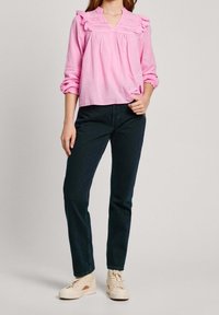 Blusa de manga larga rosa con borde rizado y diseño de escote en V, combinada con jeans oscuros y zapatillas de colores claros. Textura plana en general.