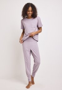 Conjunto de loungewear en color lila que consiste en una camiseta de manga corta con un bolsillo en el pecho y pantalones ajustados con puños elásticos en los tobillos, que presentan una textura suave.