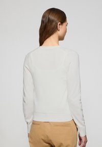 Suéter blanco ligero con mangas largas, cuello redondo y dobladillo acanalado. Textura suave, diseño ajustado y detalles minimalistas en la parte posterior.