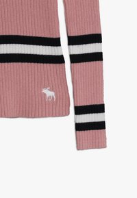 Maglione a coste rosa con strisce nere e bianche. Presenta un piccolo logo di un alce bianco in basso a sinistra.