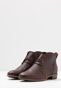 Stivali alla caviglia in pelle marrone con una texture liscia, punta tonda e minimal lacing. Presentano un piccolo tacco e sottili dettagli cuciti.