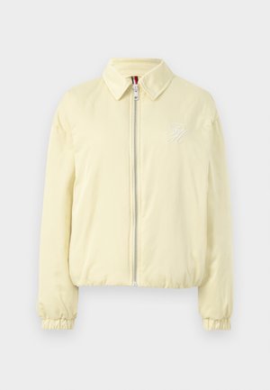 Svetlo rumena bomberska jakna z zadrgo, elastičnimi manšetami in subtilnim vezenim logotipom na prsih. Gladka tekstura tkanine.