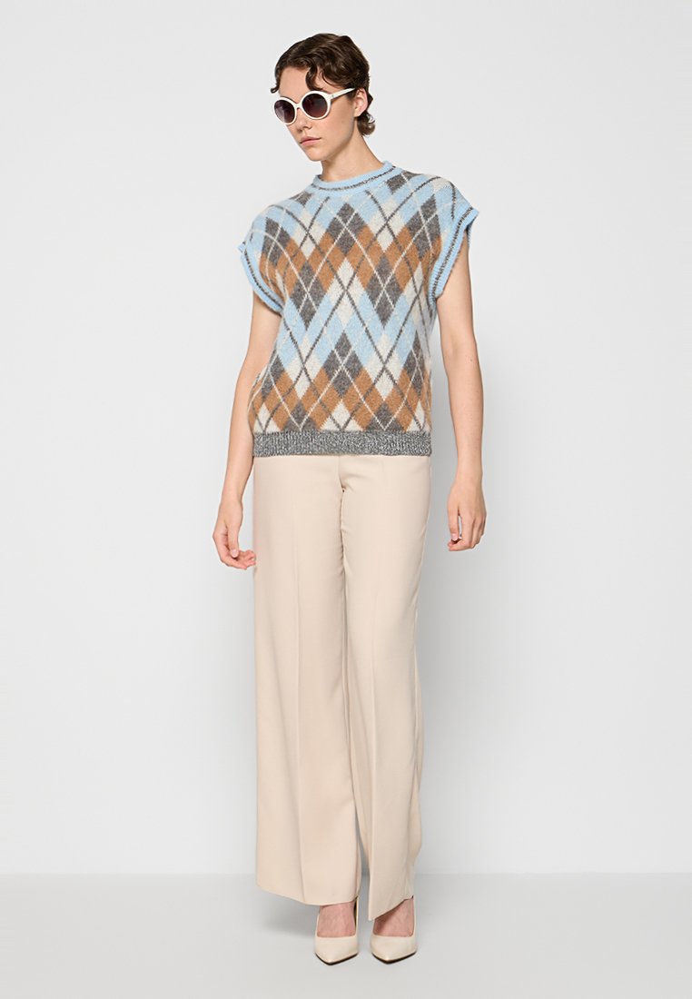 Maglione senza maniche lavorato a maglia con motivo argyle blu, marrone e grigio. Abbinato a pantaloni beige a gamba larga e occhiali da sole rosa.