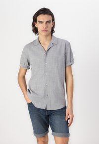 Chemise gris à manches courtes avec un tissu texturé, col ouvert et coupe décontractée, associée à un short en denim bleu retroussé.