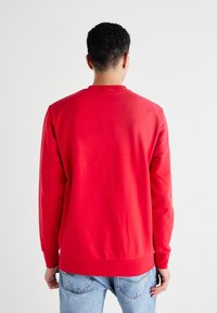 Sudadera roja de manga larga, con cuello redondo y dobladillo acanalado. Textura suave, diseño sencillo, combinada con jeans azul claro.