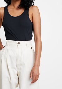 Ribbed black tank top with wide neckline paired with high-waisted cream trousers featuring dual button closures and side pockets.