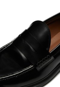Schwarze Lederloafer mit glatter Oberfläche, dekorativem Riemen und Stickereien. Das Innere ist hellbraun mit einer gepolsterten Sohle.
