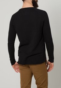 Svart långärmad skjorta med en figursydd design, mjuk textur och raglanärmar, med en rundad nederkant och minimalistisk stil.