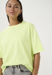 Neon yellow oversized t-shirt with a round neckline and short sleeves, paired with grey high-waisted jeans, featuring a smooth texture.
