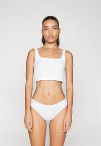 Fehér, négyzet alakú dekoltázsú, vékony pántos crop top, fehér bikini alsóval, amelynek logós derékpántja van. Sima anyagtextúra.