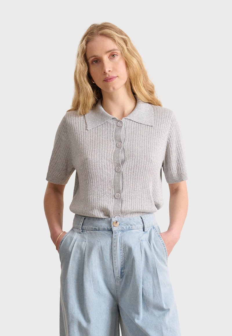 Gray ribbed short-sleeve sweater with a collared neckline, featuring a button-up front and smooth texture, paired with light blue high-waisted trousers.