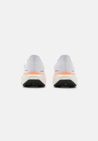 White athletic shoes with a mesh upper, orange midsole accents, and black rubber outsole, viewed from the back.