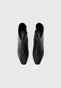 Ζευγάρι μαύρες δερμάτινες μποτάκια αστραγάλου με πλαϊνά φερμουάρ, μυτερές μύτες και πάτους με την ένδειξη "ANNA FIELD", σε θέαση από πάνω σε λευκό φόντο.