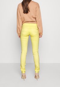 Slim-fit gula jeans i mjukt tyg med bakfickor som har en rundad design. Kombinerat med en beige tröja och neutrala klackar.