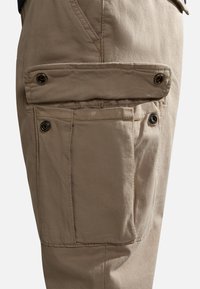 Beige cargo broek met een grote zijzak, knopen voor een veilige sluiting en een gestructureerde stofafwerking.