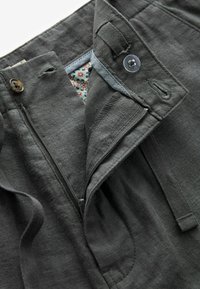 Pantalons en lin gris foncé avec une fermeture éclair, un bouton, et une doublure à motifs floraux. Comprend des poches sur les côtés et un détail de taille ajustable.