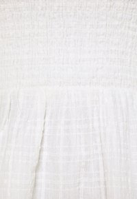 Bílá smocked šaty s texturovaným povrchem a jemným mřížkovým vzorem, které mají splývavou sukně a jemnou tkaninu.