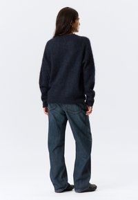 Pull en laine moelleux bleu marine, avec une coupe décontractée, des poignets côtelés et un col rond simple, associé à un jean en denim bleu ample.