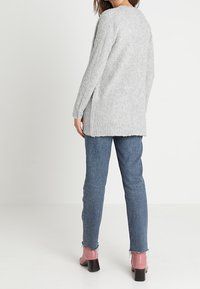 Maglione a maglia grigia chiara con maniche lunghe, vestibilità rilassata e bordi a coste, indossato sopra jeans blu e stivaletti rosa con tacco.